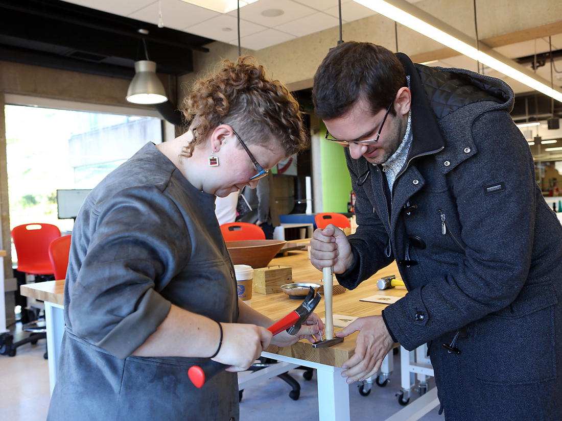 A man and woman work together on an innovative project on a wooden table with hammers.