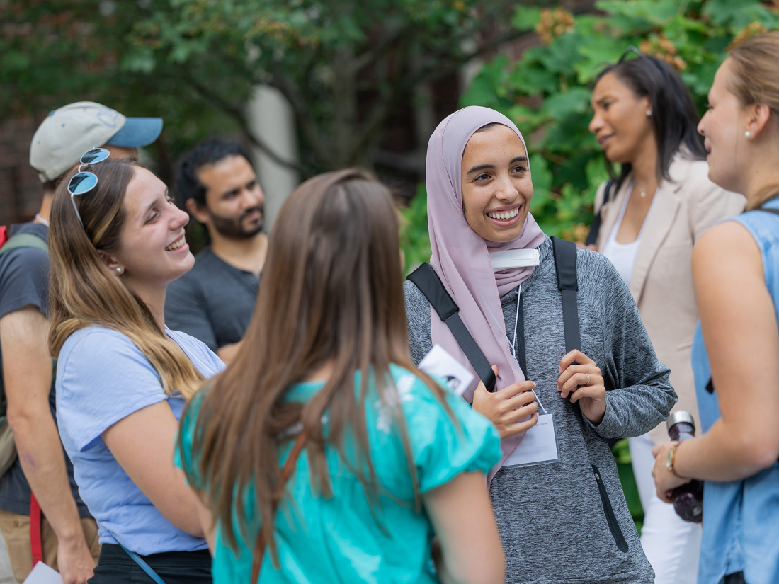 A group of students and faculty smile while discussing things outside.