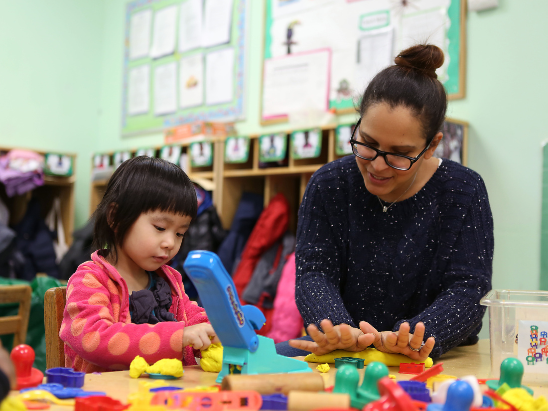 Educator plays play dough with child in preschool classroom.