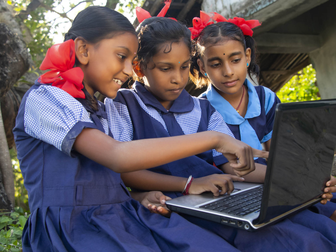 Three schoolgirls from India look at materials on a laptop